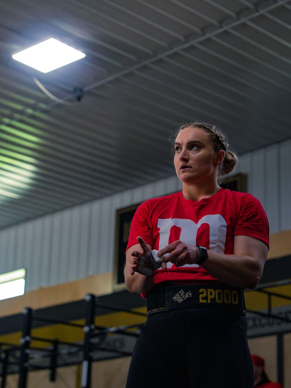 CrossFit athlete in an M&M costume and lifting belt chalks her hands between sets, eyes fixed downrange as she sets up for the next lift.