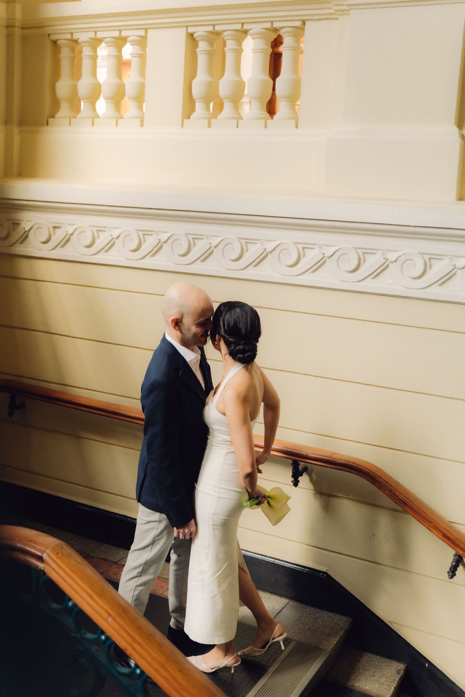 Bride and groom share a romantic kiss on a staircase landing featuring ornate molding and wooden handrail.