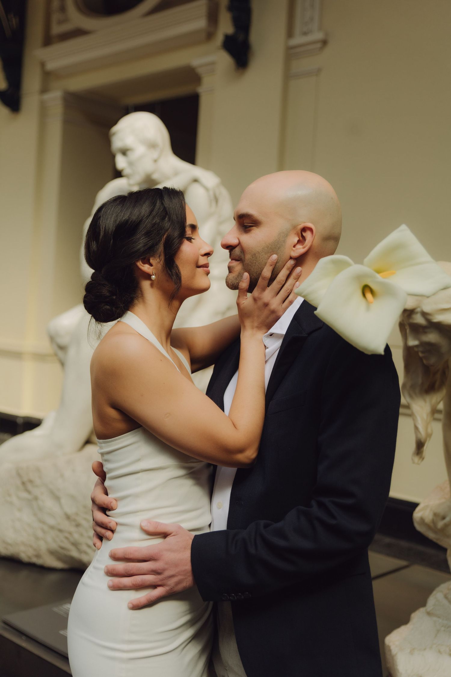 Bride and groom share a romantic moment among classical sculptures in a museum wedding venue.