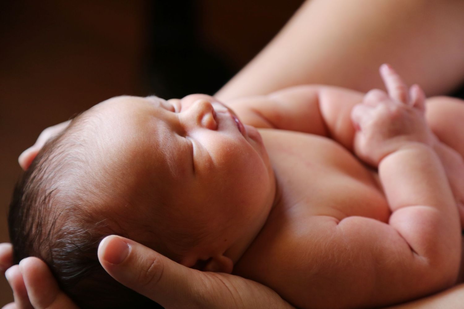 Close-up of a sleeping newborn baby cradled in a parent's hands, with tiny fingers curled near its face.