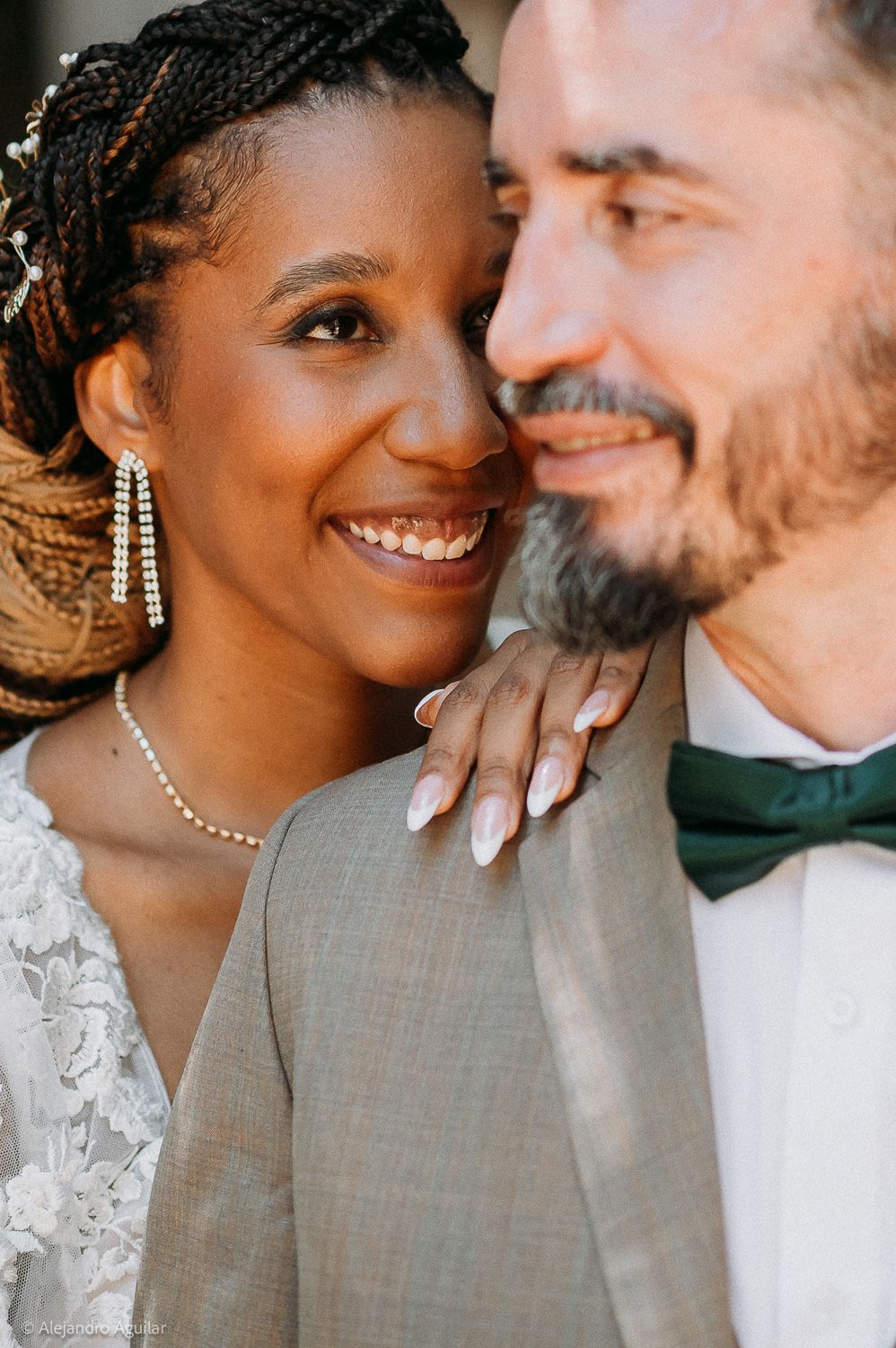 A joyful bride and groom share an intimate moment, she smiles radiantly in a lace gown with pearl earrings.