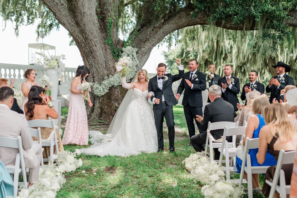 Newlyweds celebrate with raised arms as they walk back down the aisle after their outdoor wedding ceremony.