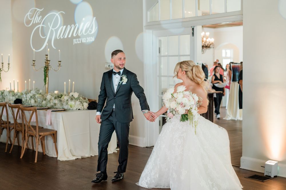 Newlyweds make grand reception entrance under a glowing monogram sign reading The Ramies at elegant venue.