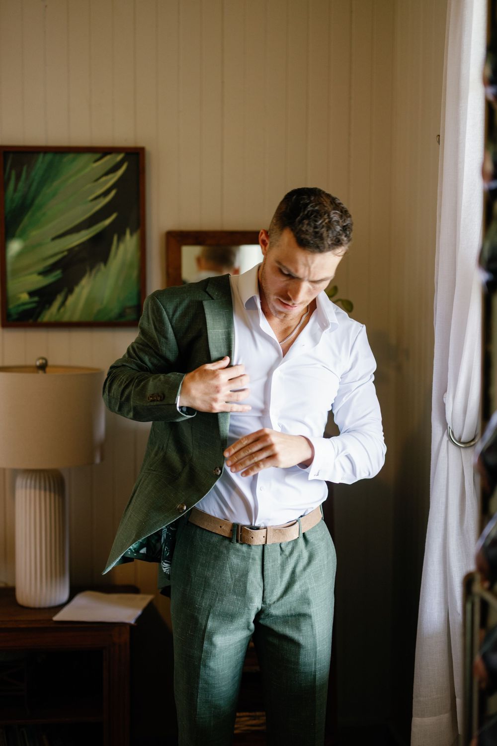 Groom in green suit adjusting cufflinks while getting ready for wedding ceremony.