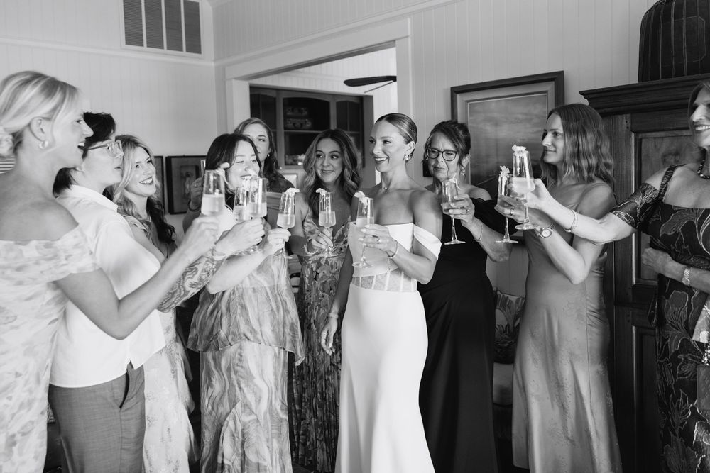 Bride and bridesmaids toasting with champagne glasses in black and white photo.