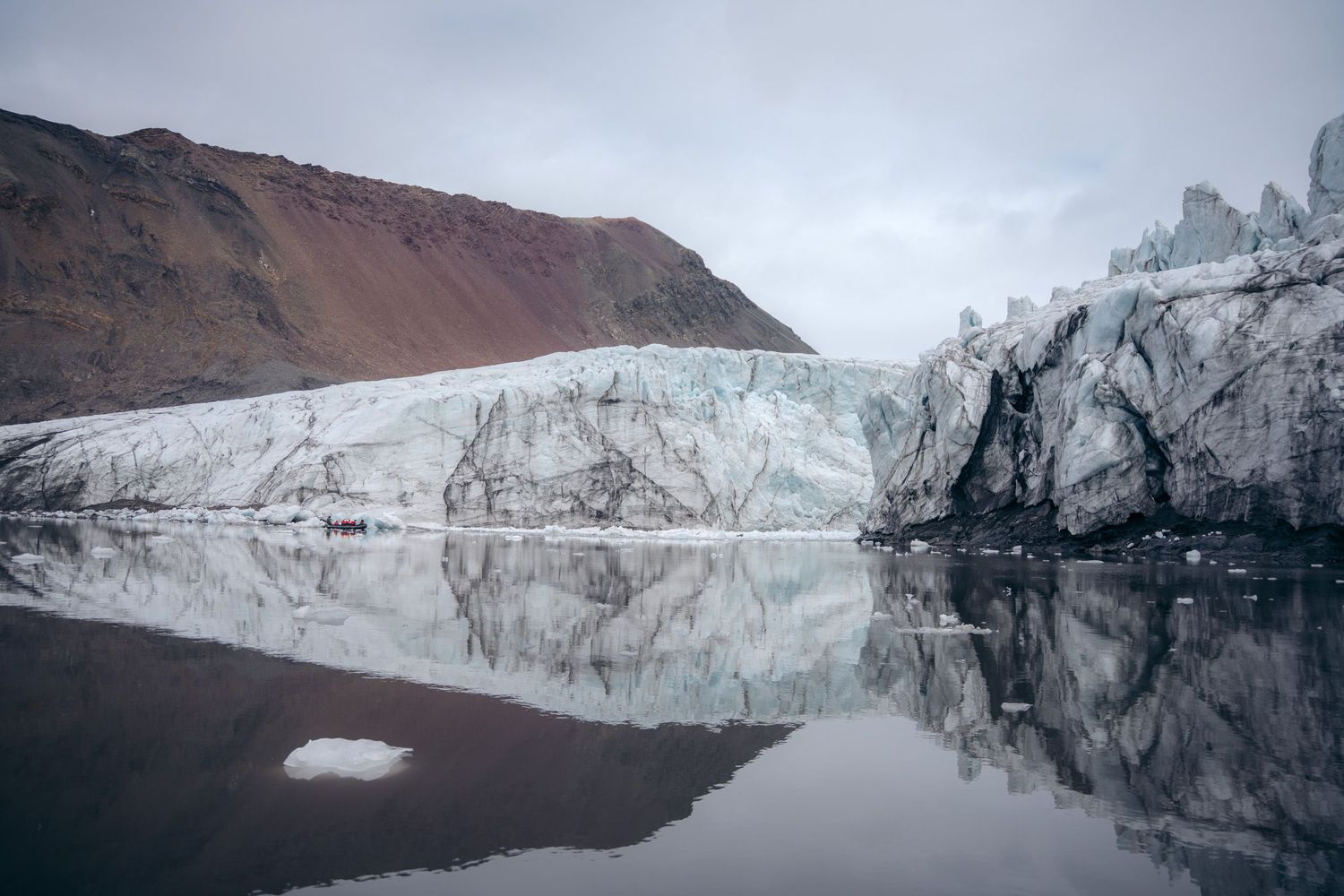 Front glaciaire parfaitement reflété dans l'eau, zodiac minuscule à son pied