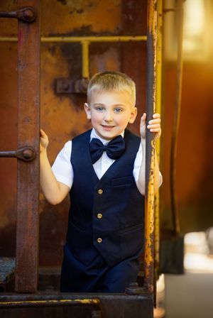 A formal black vest and bowtie outfit photographed through rustic metal bars in warm lighting.