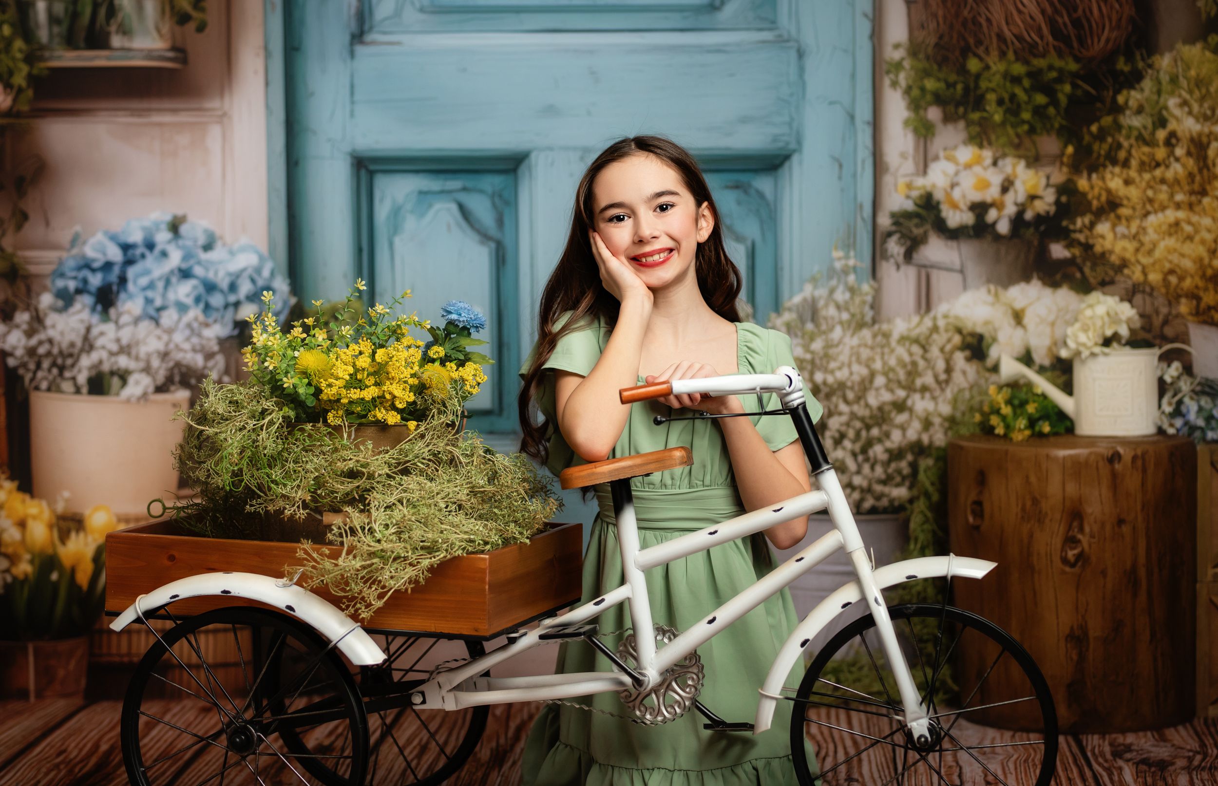 A vintage-style mint green bicycle with a wicker basket stands against a rustic wooden fence in a garden setting.