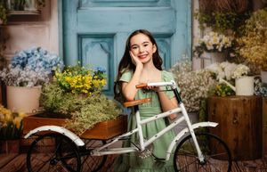 A vintage-style mint green bicycle with a wicker basket stands against a rustic wooden fence in a garden setting.
