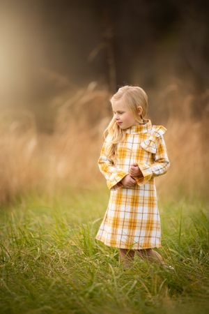 Serene outdoor portrait in yellow plaid dress amid tall autumn grasses.