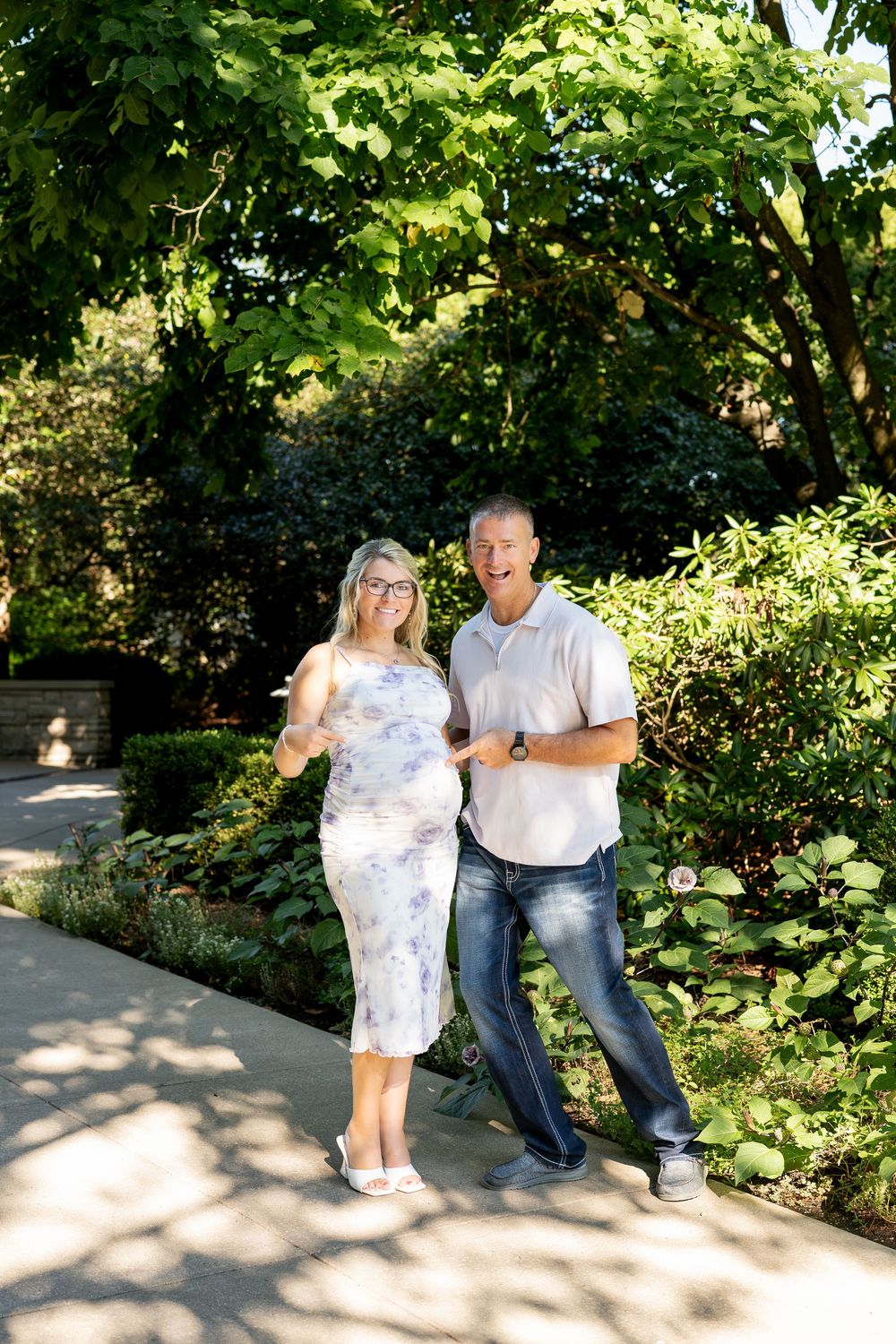 Happy couple smiling together on a garden path surrounded by lush green trees and shrubs on a sunny day.