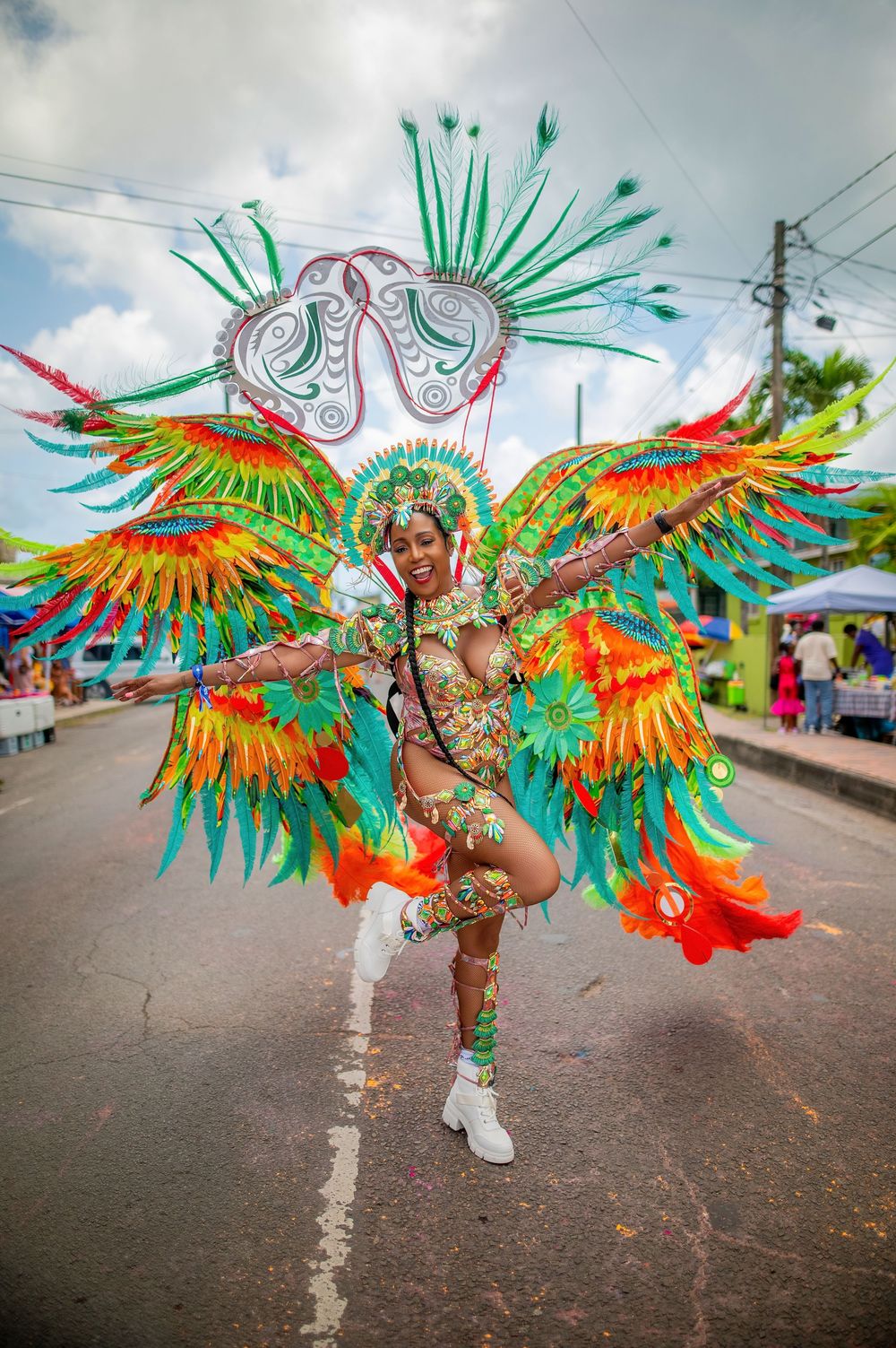Vibrant carnival performer in colorful feathered costume with wings dancing on street during festive parade celebration.
