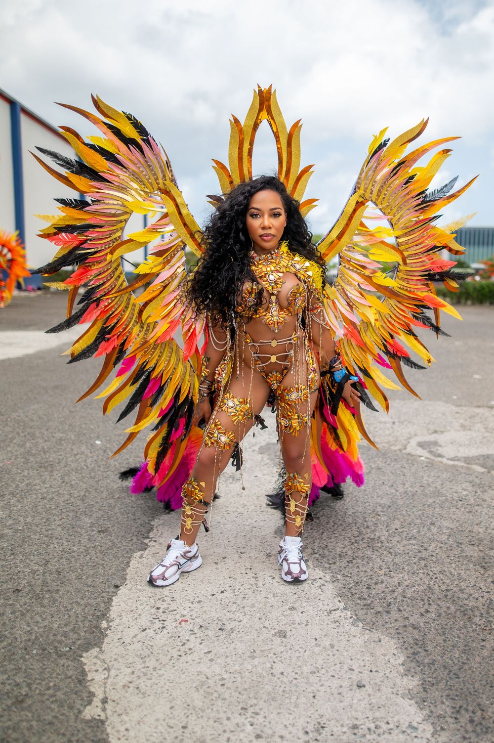 Woman in elaborate golden feathered carnival costume with large angel wings poses on street during festival.