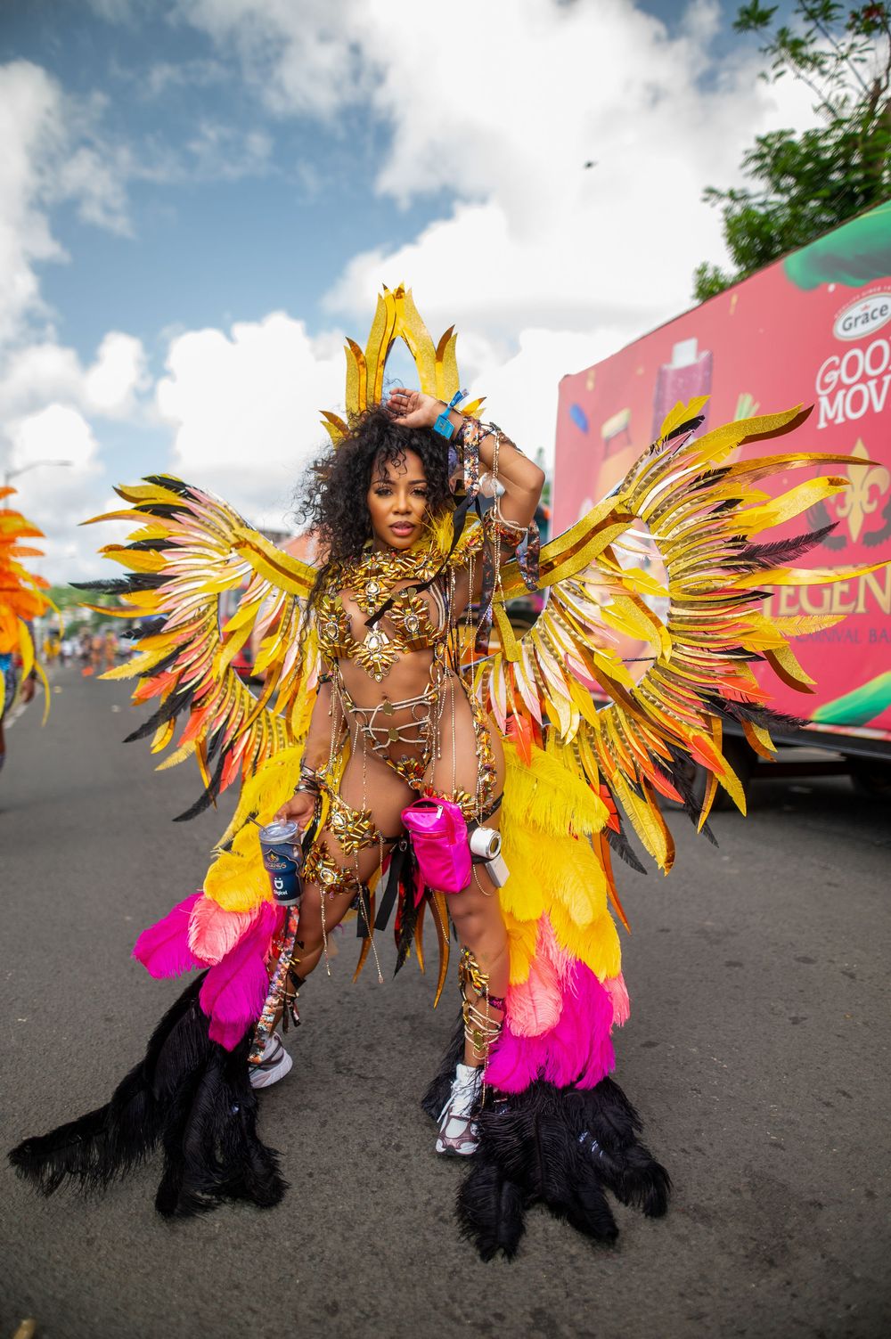 Woman in vibrant yellow and pink feathered carnival costume with wings poses during a colorful street parade.