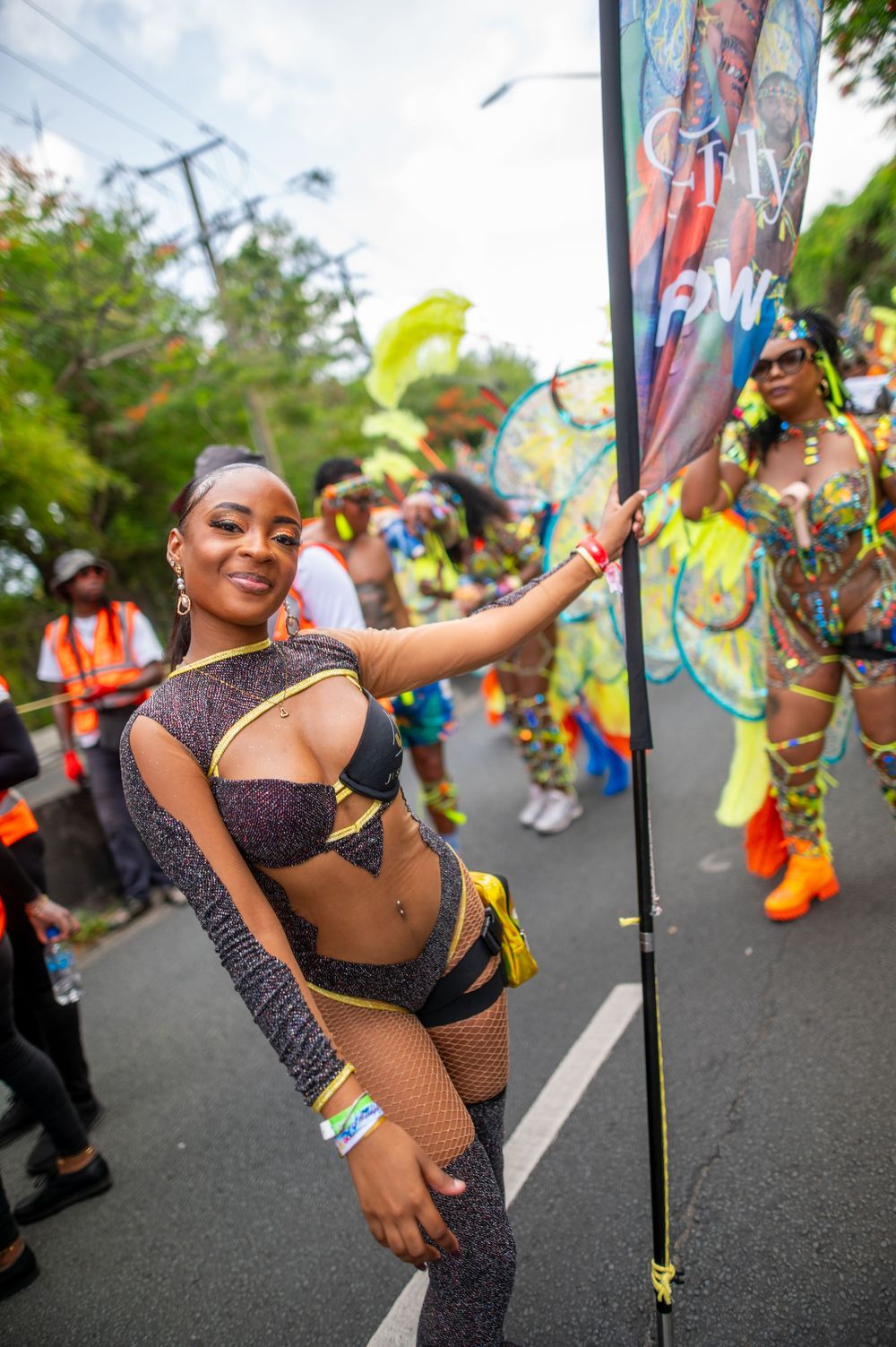 Woman in carnival costume poses at a vibrant street parade with colorful festival performers behind her.