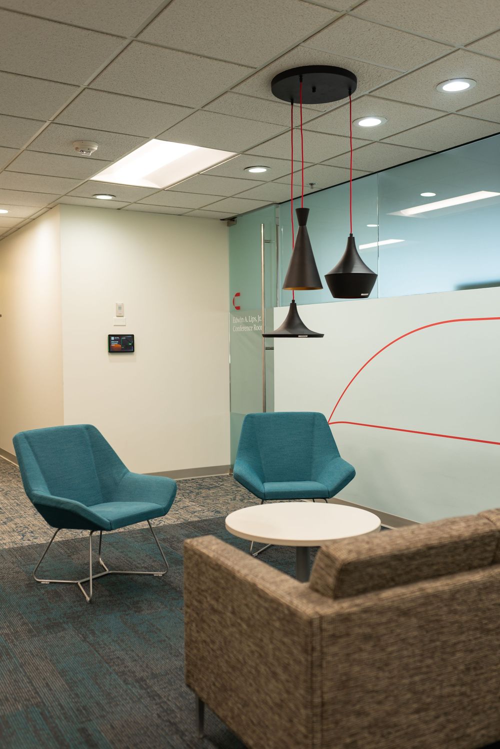 Modern office lounge with teal chairs, white coffee table, pendant lights, and glass partition wall.