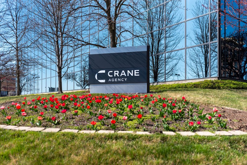 Crane Agency office building sign surrounded by vibrant red tulips in a landscaped garden during spring.