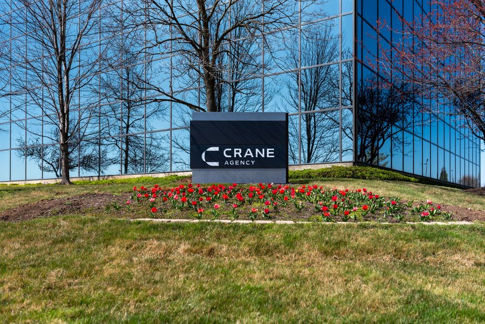 Crane Agency office building exterior sign with red tulips and reflective glass facade on a sunny spring day.