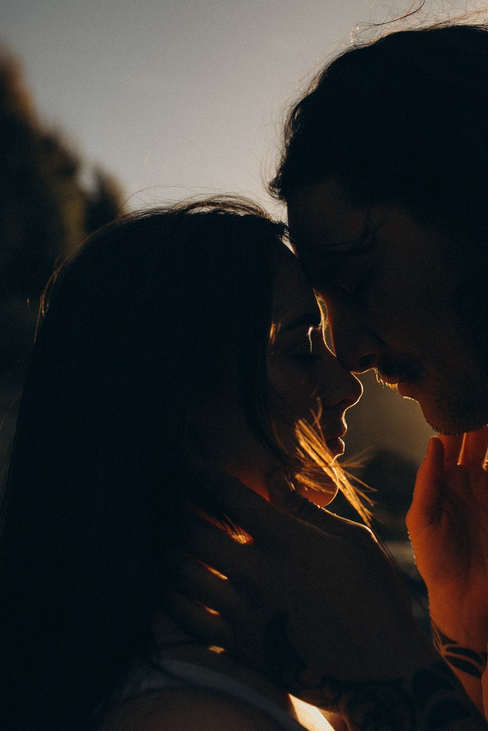 Two people share a romantic moment at golden hour, their faces close together in warm backlit sunlight.