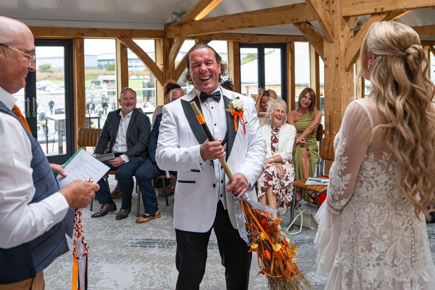 Groom in white tuxedo laughing during wedding ceremony with bride in elegant lace dress.Yorkshire, Sheffield, Lincolnshire, UK