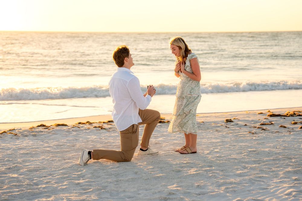Romantic beach marriage proposal at sunset, man kneeling with ring before emotional woman.