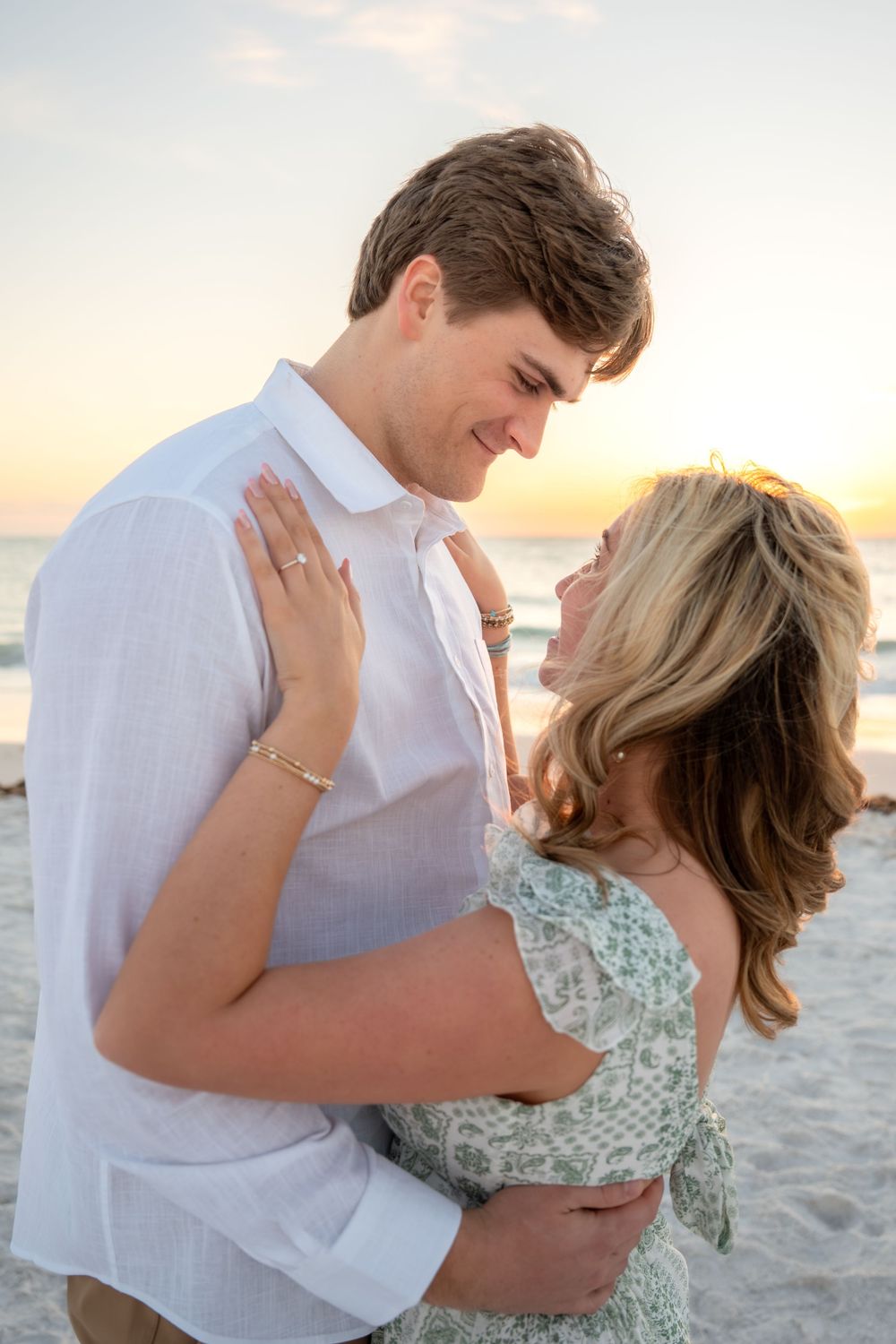 Romantic couple gazing into each other's eyes at beach sunset, embracing in soft golden light on the shore.