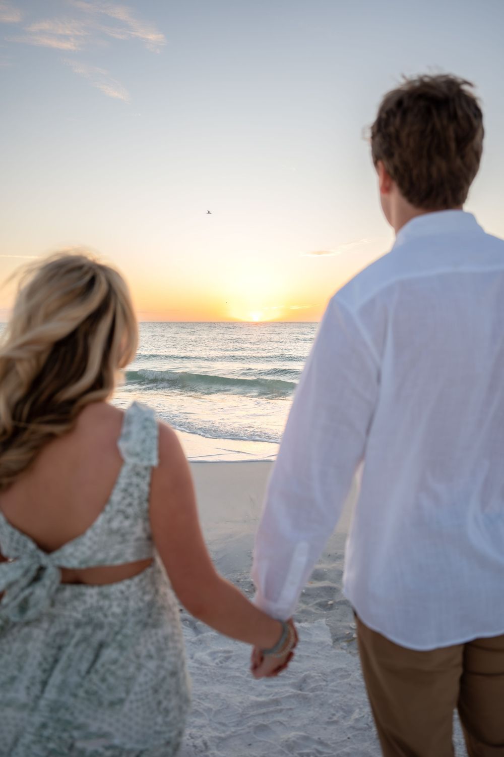 Couple holding hands facing the ocean at a breathtaking beach sunset, viewed from behind in romantic pose.