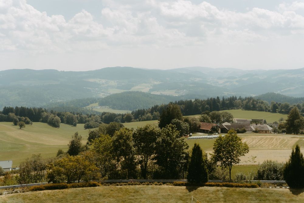 Scenic rolling green hills with trees and farmhouses in a peaceful countryside valley landscape.