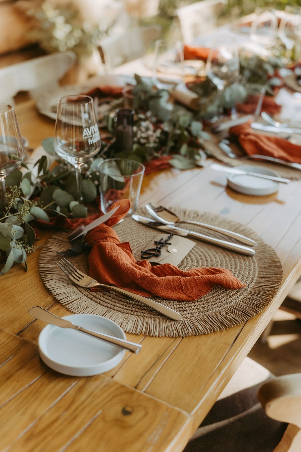 Rustic wedding table setting with terracotta napkins, eucalyptus greenery, and woven placemats.