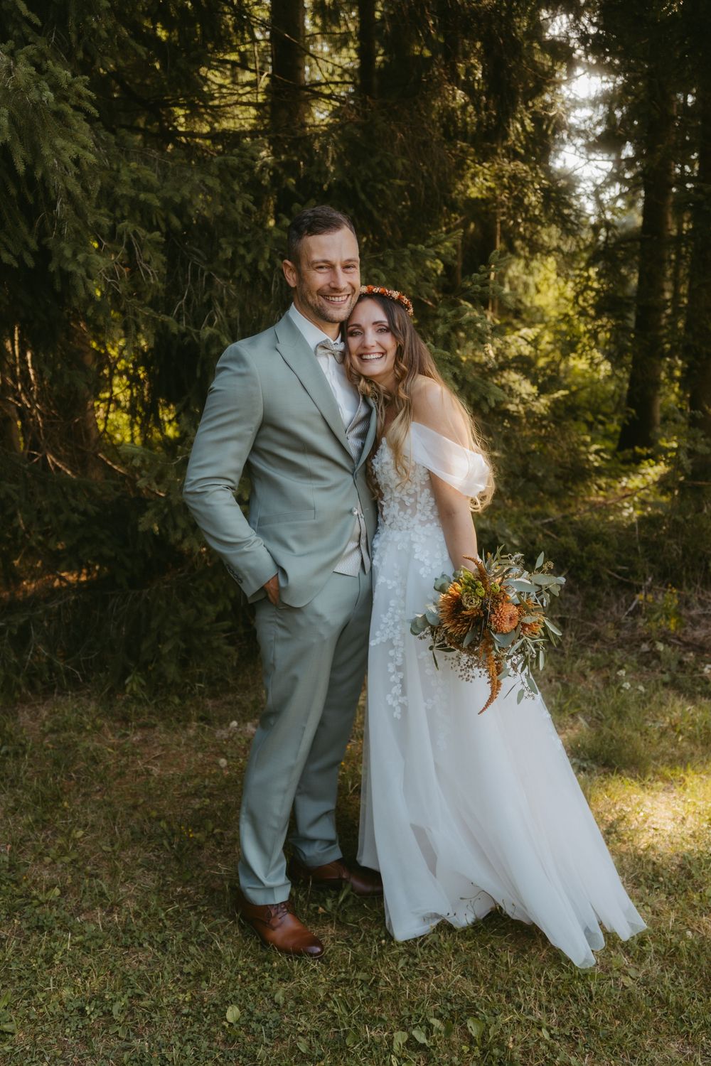 Happy bride and groom posing together in a sunlit forest, bride holding autumn bouquet.