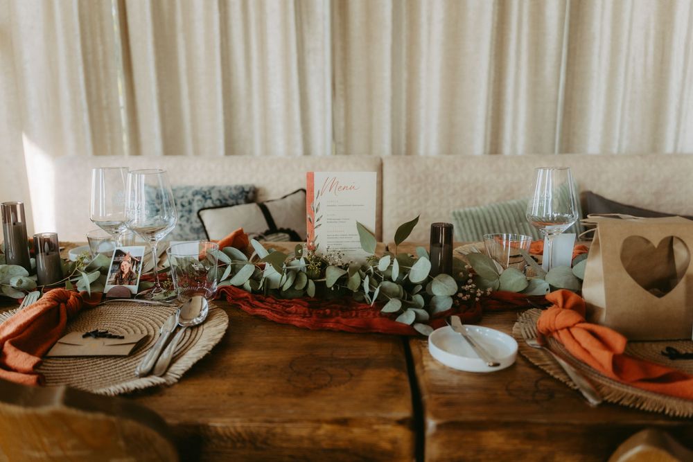 Rustic wedding reception table setting with eucalyptus greenery, terracotta napkins, wicker chargers, and elegant glassware.