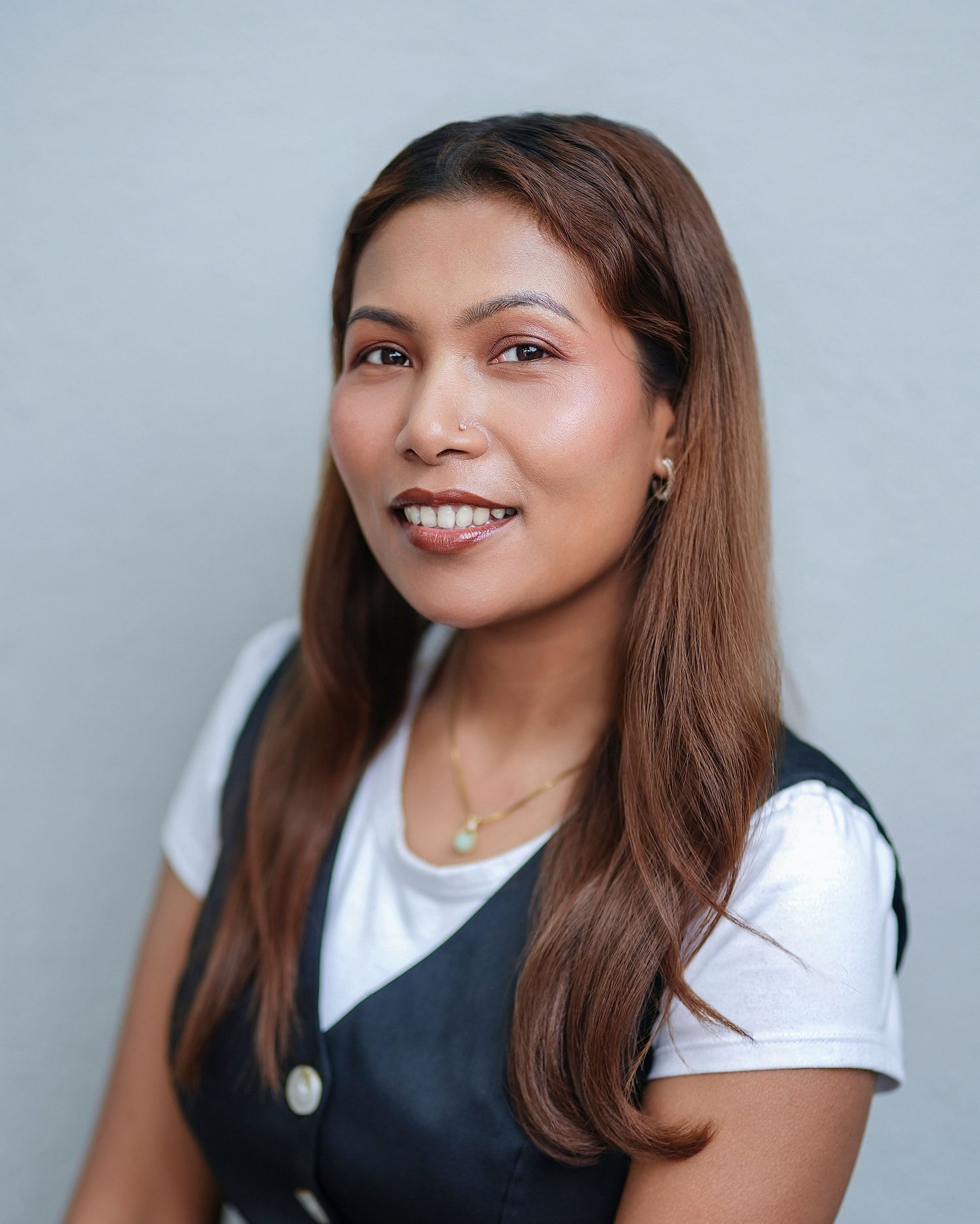 Professional headshot of a smiling brunette woman in a striped blouse on a gray background.