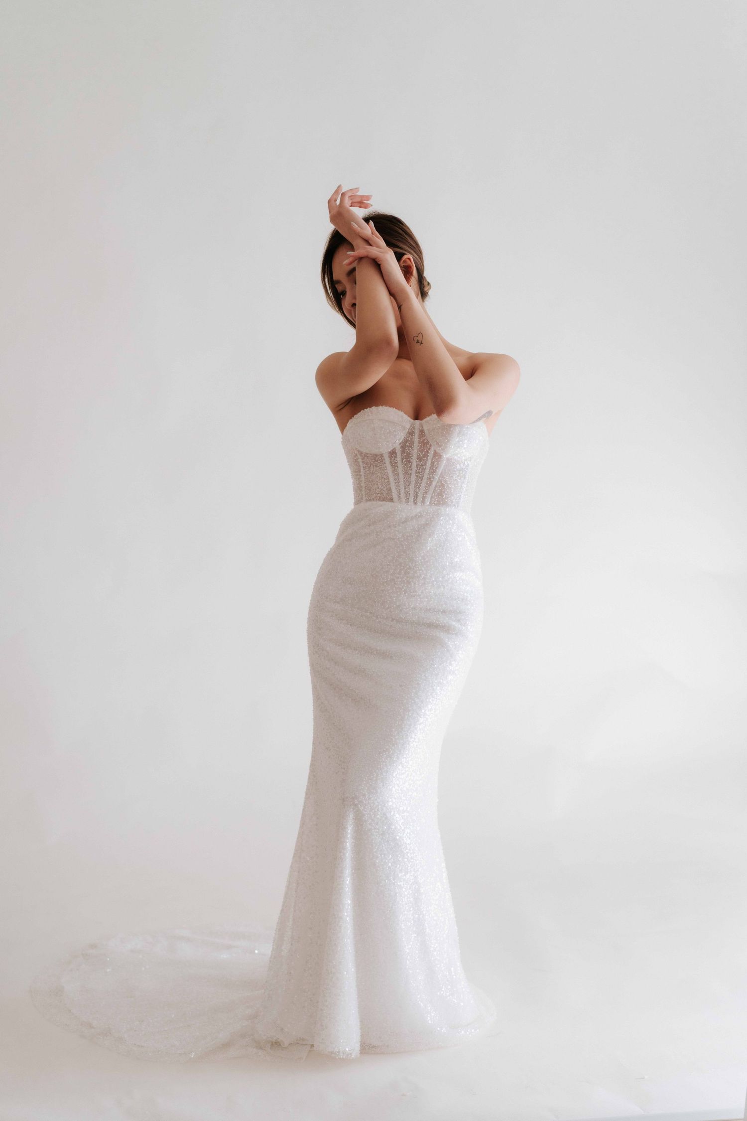 Person in white fitted wedding dress posing against light background.