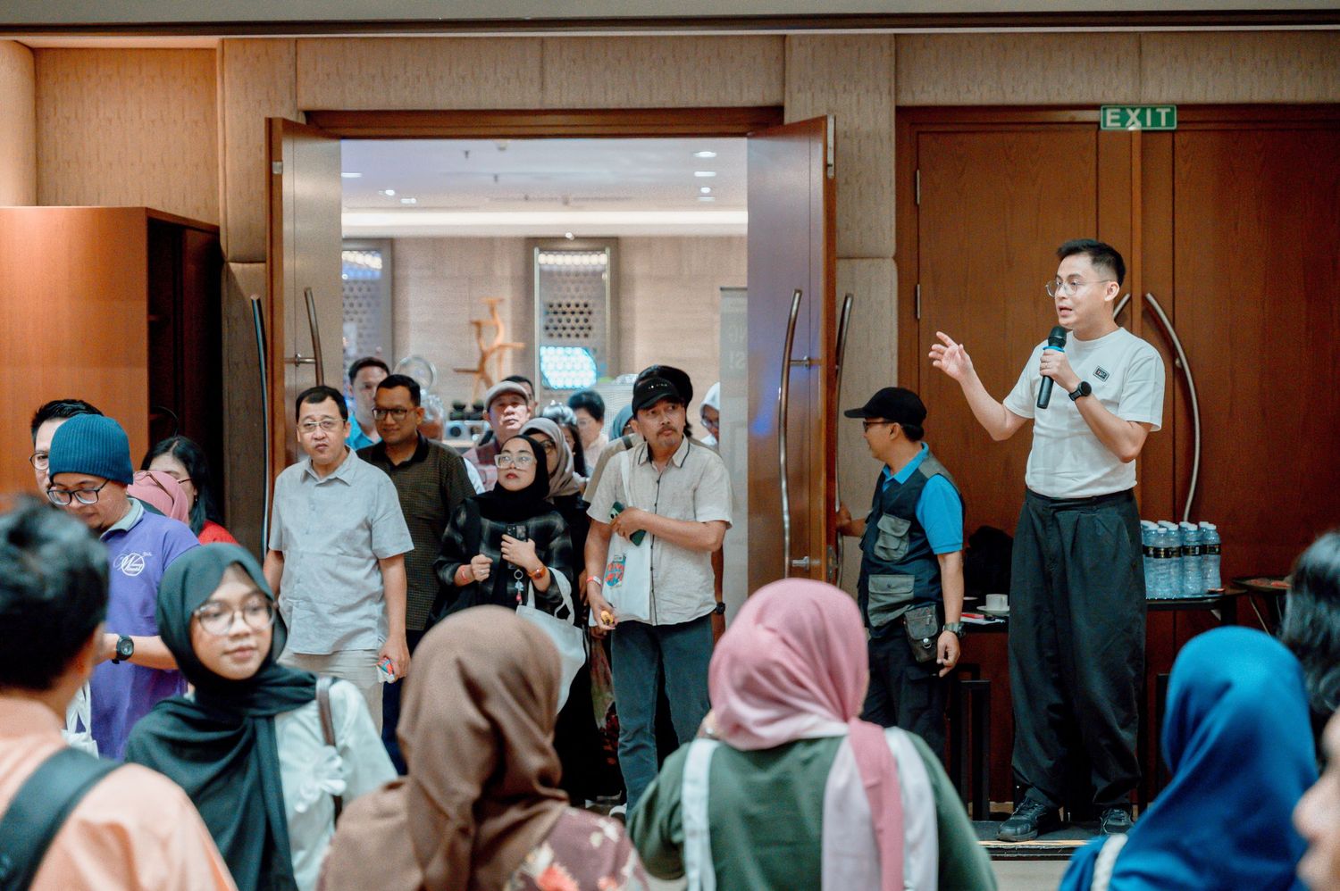 A man addresses a crowd in a hotel lobby during a group event in Southeast Asia.