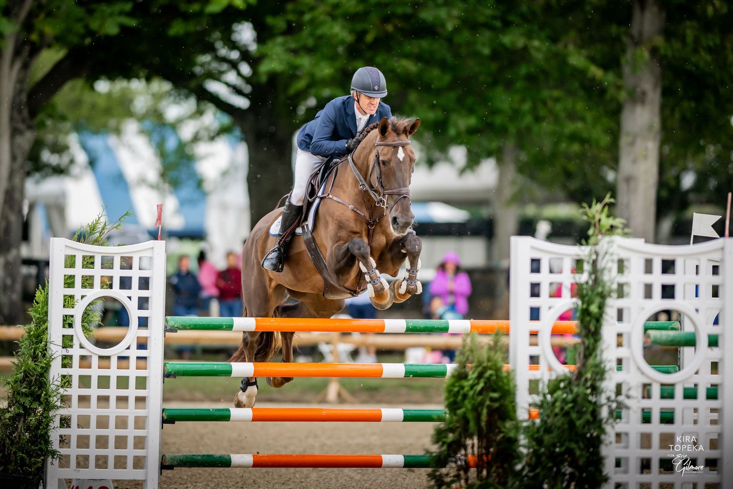 Young equestrian rider on black horse poses with ribbons and smiling woman at outdoor horse show competition.