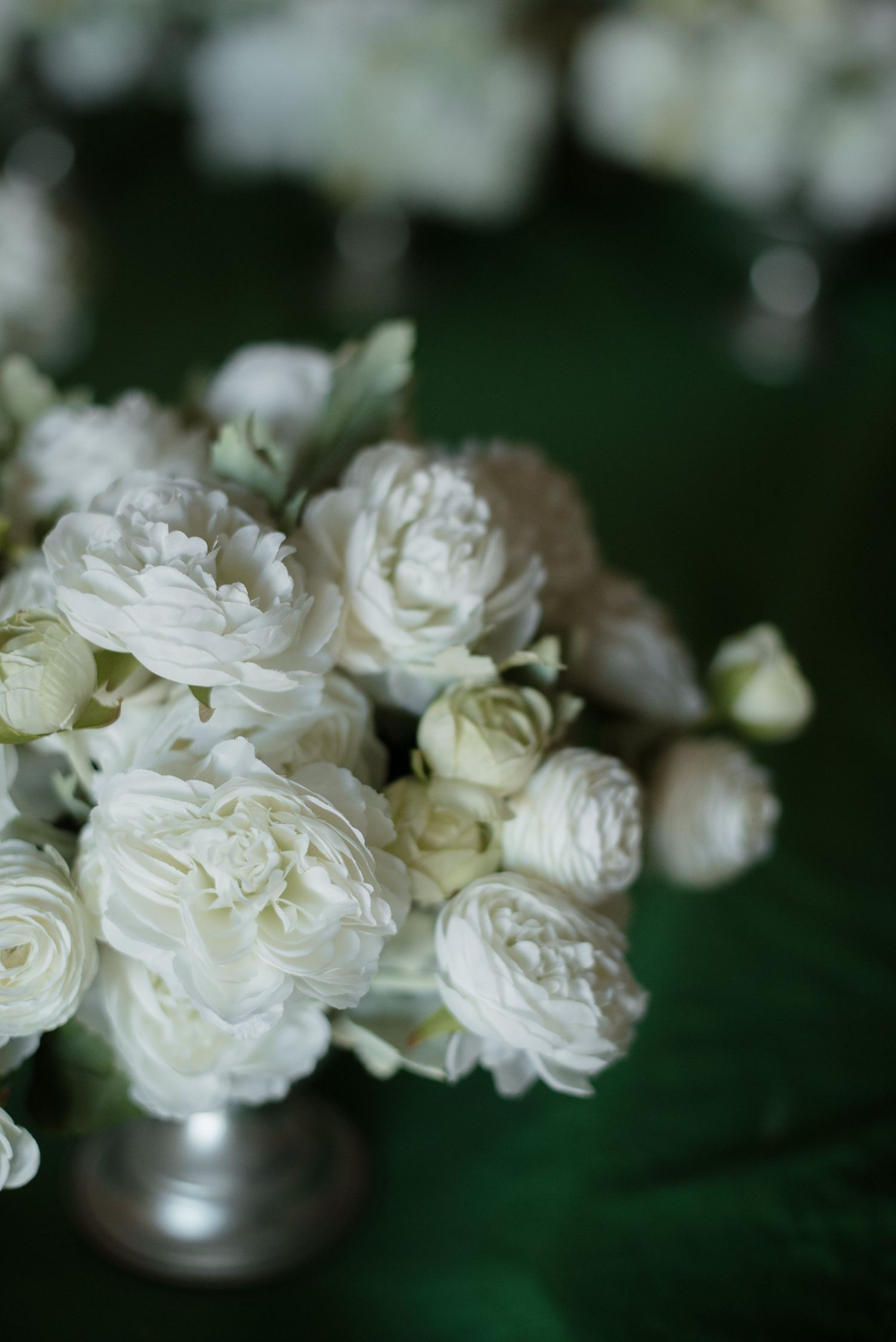 Elegant white peony and rose bouquet arrangement in a silver vase on a green velvet table.