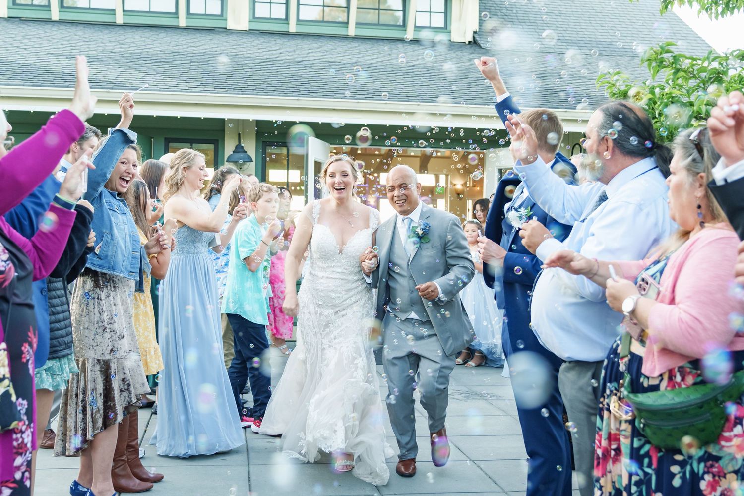 Bride and groom walk through cheering guests tossing confetti at outdoor wedding celebration.