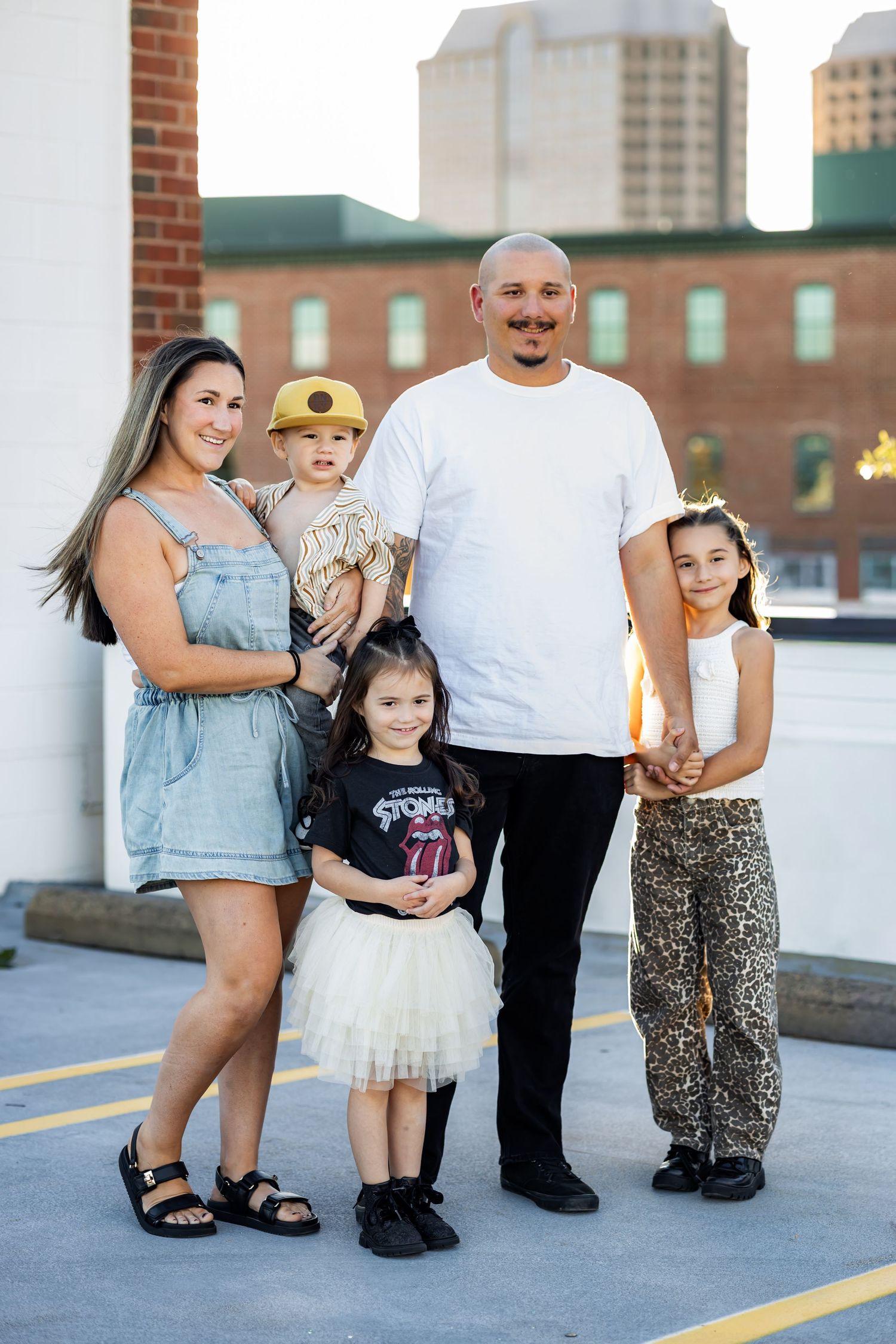 Family of five posing together on rooftop with urban buildings in background on sunny day.