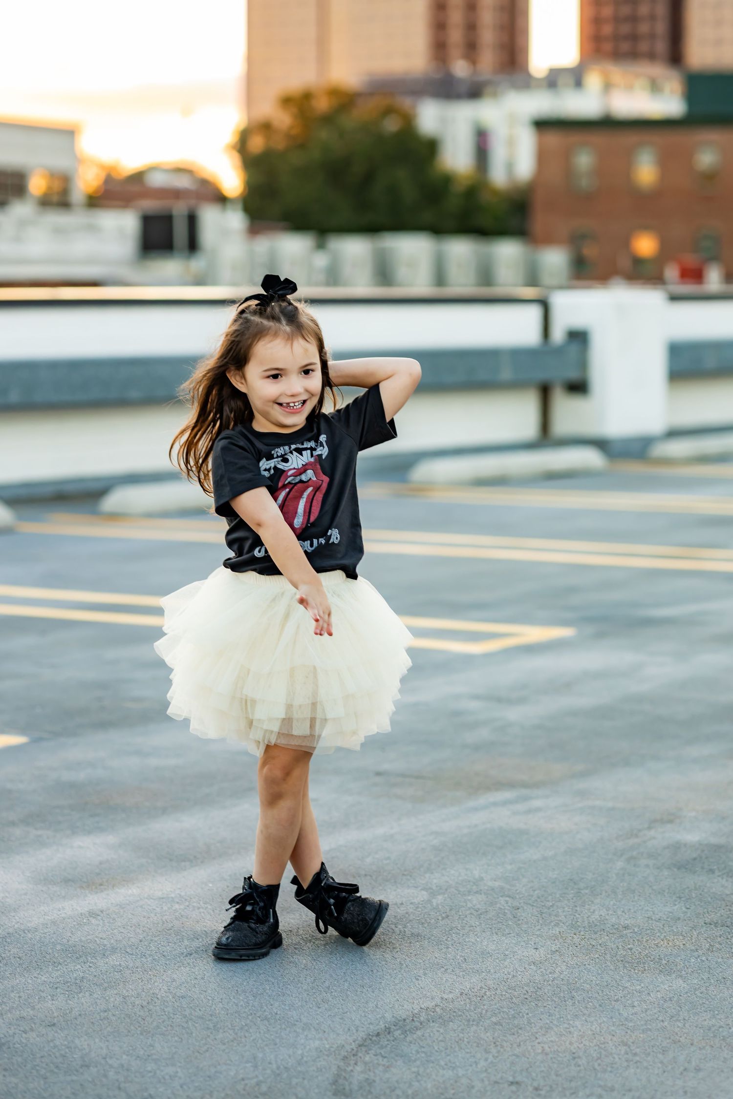Young girl in Rolling Stones tee and white tulle skirt poses on rooftop parking lot at golden hour.