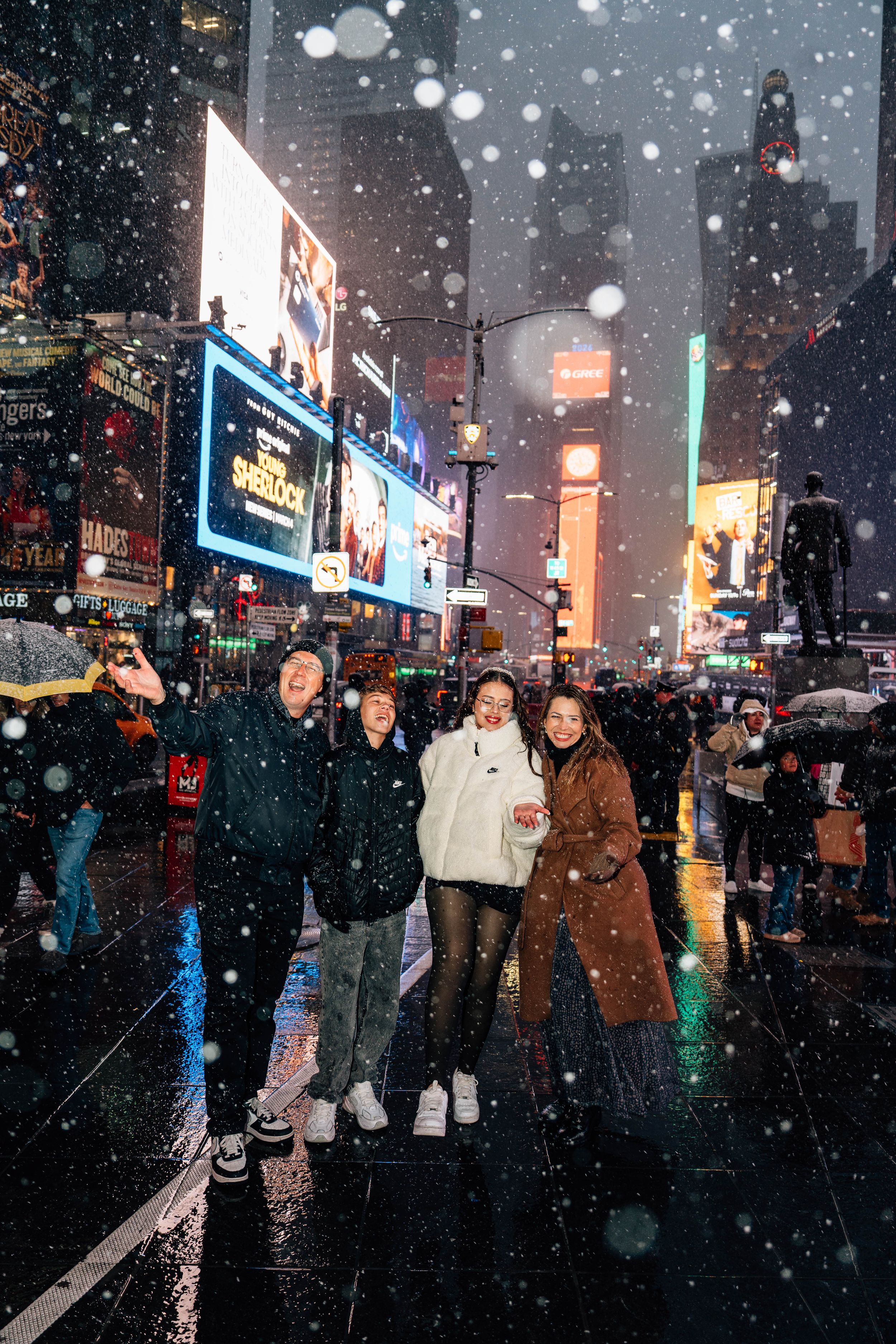 Four friends pose joyfully in snowy Times Square NYC at night, surrounded by bright billboards and city lights.