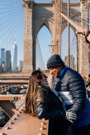 Romantic couple sharing a moment on the iconic Brooklyn Bridge on a sunny winter day.