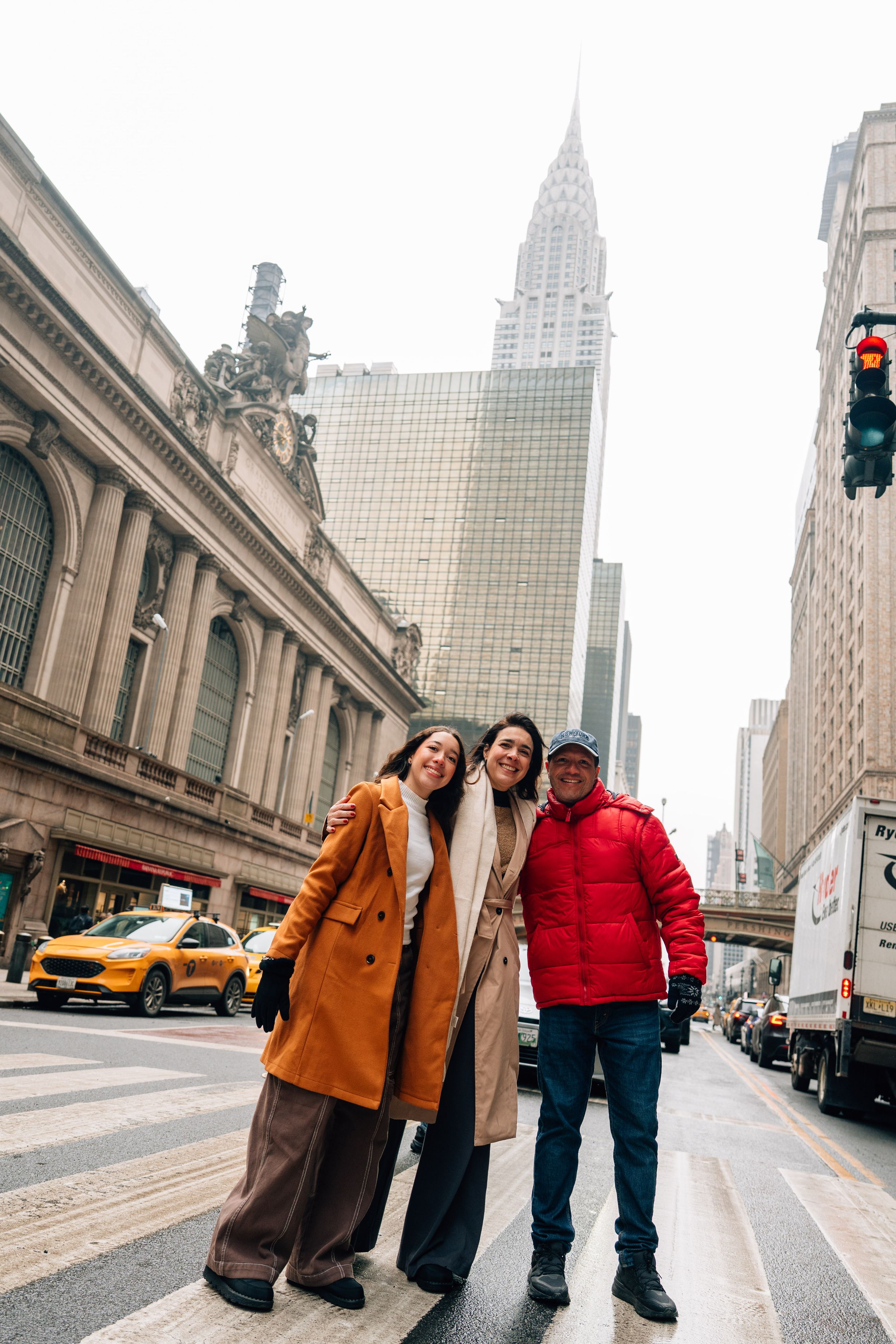 Three friends pose on a crosswalk in New York City with the Chrysler Building and Grand Central Terminal in the background.
