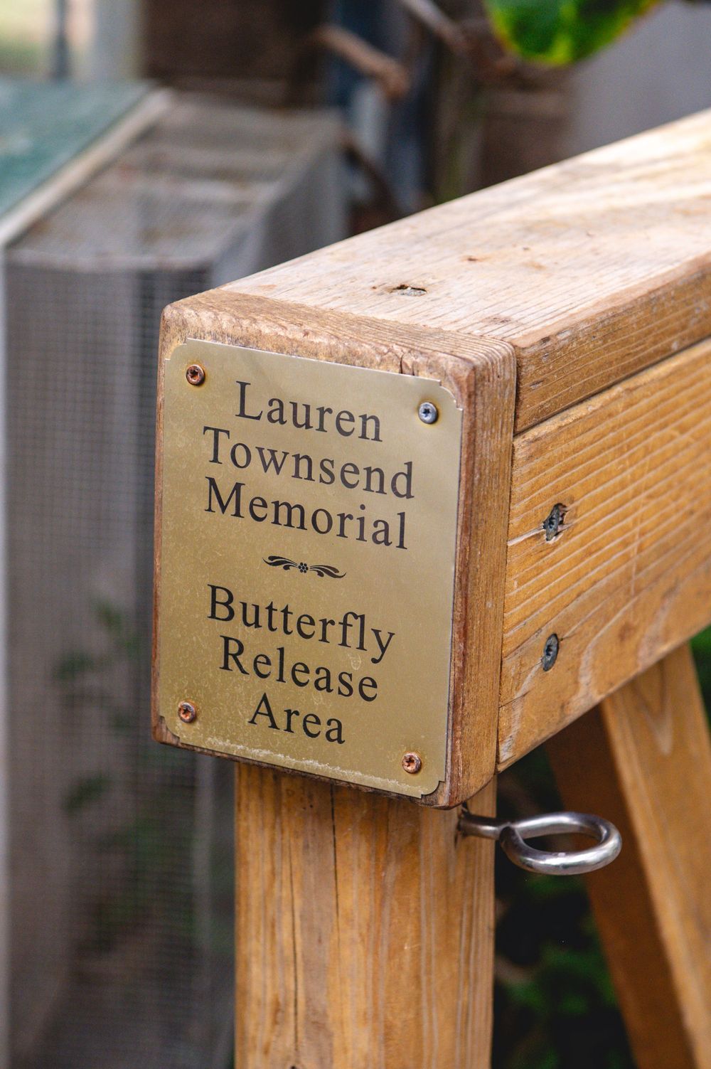 Brass plaque on wooden post marking the Lauren Townsend Memorial Butterfly Release Area in a garden setting.