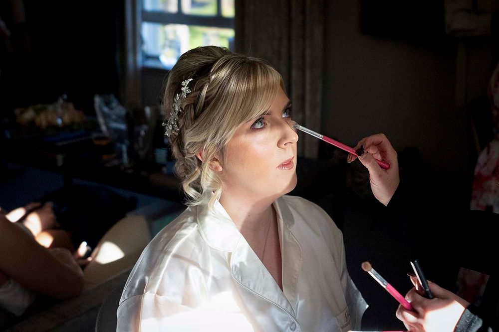 Abbie dressed in a white robe getting makeup applied prior to her  Hetland Hall wedding at Christmas time