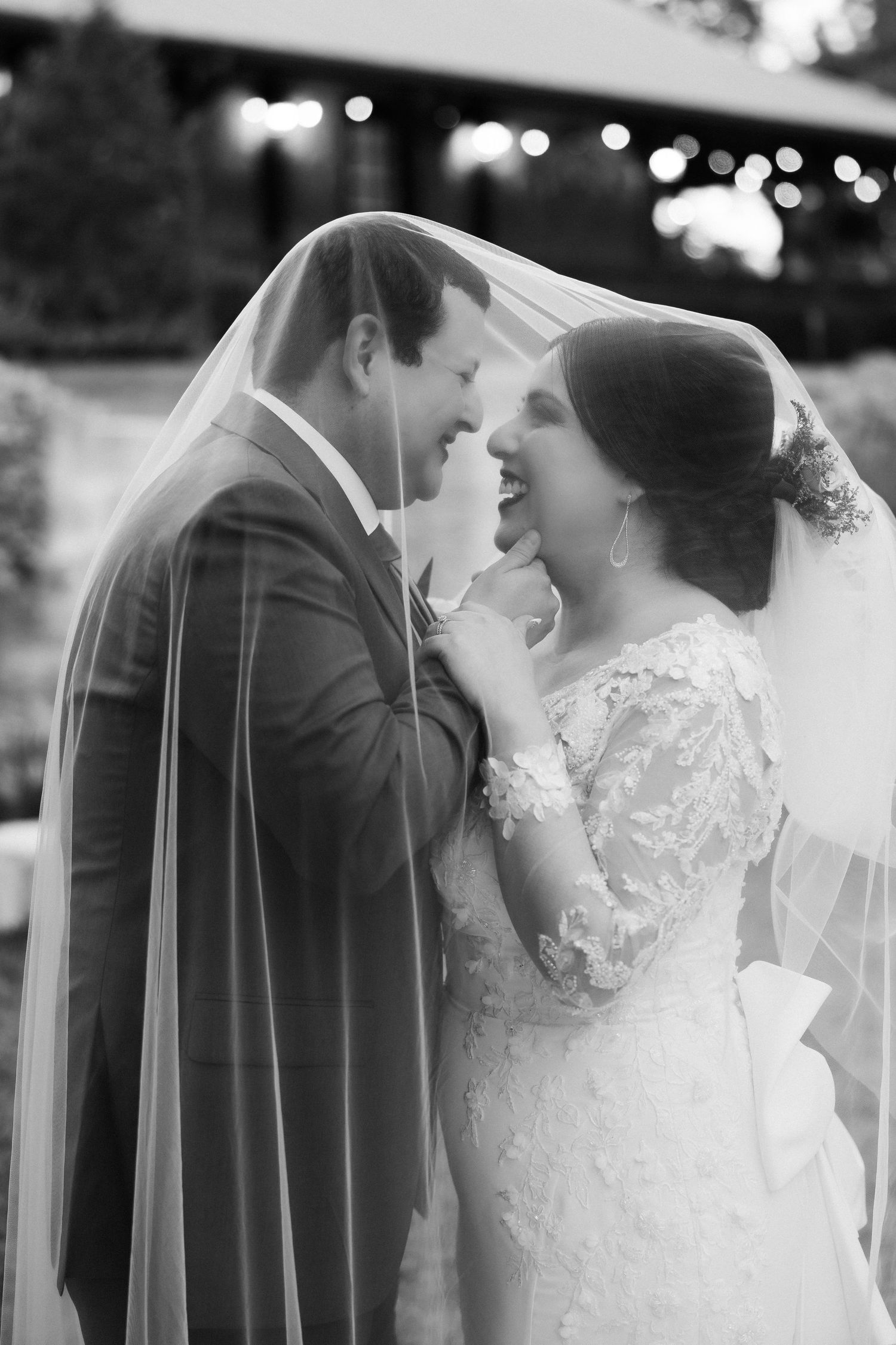Black and white photo of bride and groom sharing a joyful moment under her veil on their wedding day.