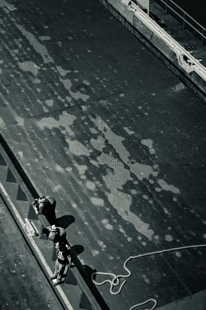 Black and white aerial view of a worker with safety rope standing on a large industrial rooftop surface.