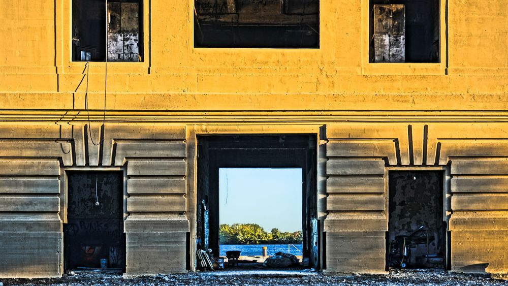 Yellow historic building facade with large archway revealing a scenic waterway and trees beyond.