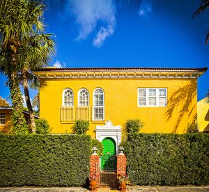 Vibrant yellow Mediterranean-style home with green door, ivy hedges, and arched windows under a bright blue sky.