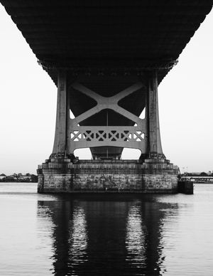 Black and white photo of a massive bridge support pillar rising from calm water, showcasing industrial architecture.