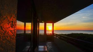 Stunning sunset view from a covered balcony overlooking the ocean with vibrant orange and red sky.